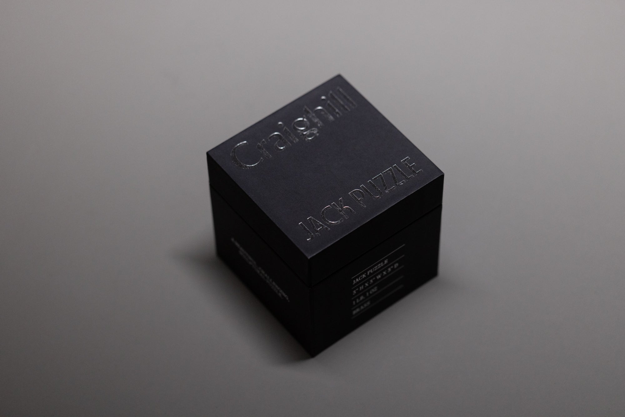 A black cube-shaped box with Craighill and Jack Puzzle embossed on the lid, placed on a plain gray surface.