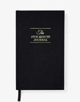 The Five Minute Journal by Intelligent Change is a sleek black hardcover featuring gold lettering and a black ribbon bookmark. With 264 undated pages, this journal offers flexible planning over any 6-month period against a plain white background.