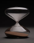 The Intelligent Change Mindful Focus 30 Minute Hourglass, featuring clear glass and brown sand mostly in the bottom half, stands centered and well-lit against a dark background—ideal for illustrating time management.
