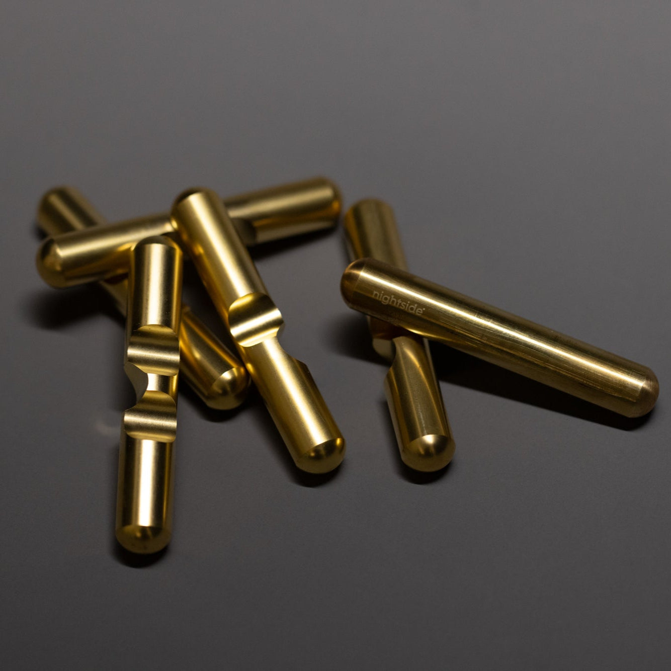 Several shiny, brass-toned metal cylinders with grooves lie scattered on a dark, reflective surface.