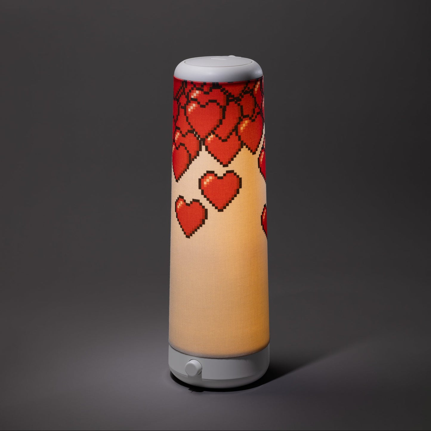The Nightside NS01 Personal Task Lamp features a cylindrical design with a white base and shade, adorned with red pixelated hearts cascading from the top, casting soothing warm-white LED light against a dark gray background.