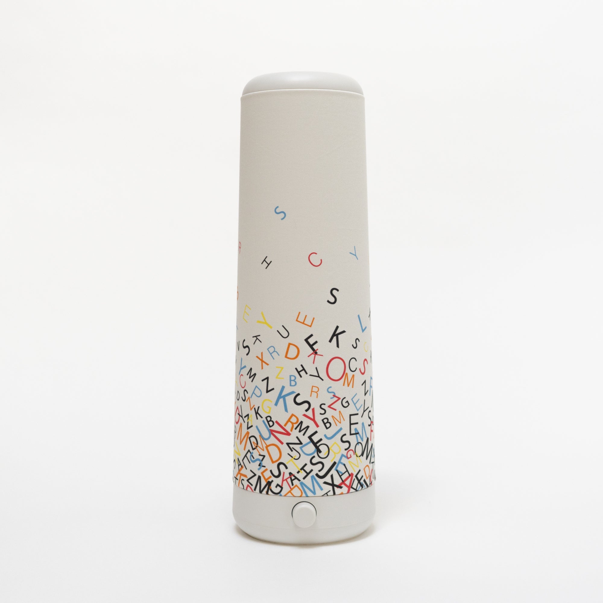 The Nightside Alphabet Cascade Cotton Shade is an off-white, tall lamp shade decorated with colorful alphabet letters that cluster at the base and spread upward. The interchangeable fabric shade allows for a customizable style.