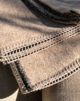 Close-up of folded Midnight Sun Throw Blankets by Blacksaw, made from eco-friendly baby alpaca. They feature intricate black and white stitching along the edges. The texture is soft and cozy, with sunlight casting gentle shadows over the hypoallergenic surface.