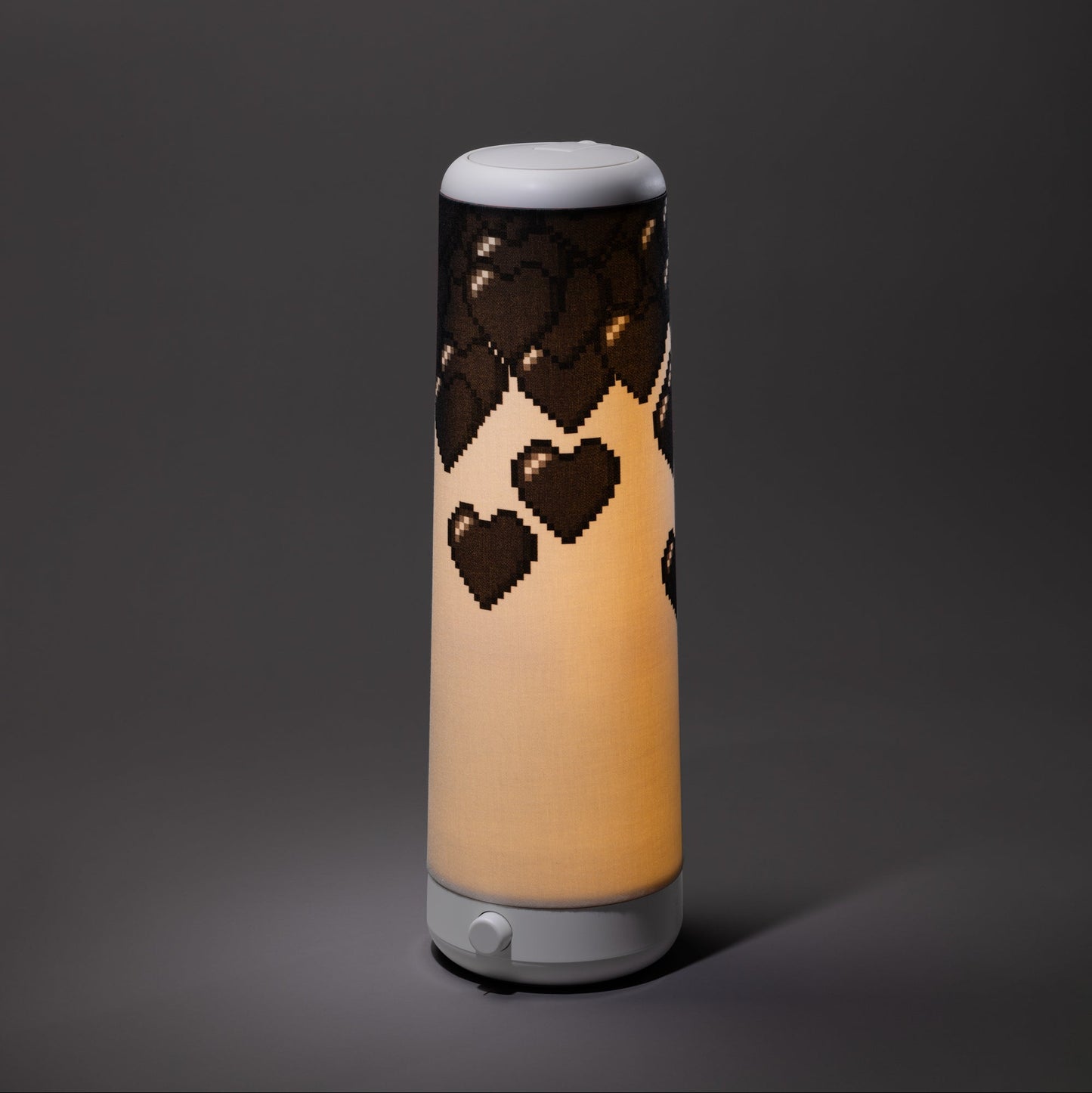 The Nightside 8-bit Hearts Cotton Shade is a cylindrical black lamp with a soft, warm glow and bold pixelated heart patterns near the top against a plain dark background.
