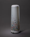 The Nightside Alphabet Cascade Cotton Shade lamp features a tall, cylindrical design with white accents and colorful alphabet letters, plus interchangeable fabric shades, displayed against a dark background.