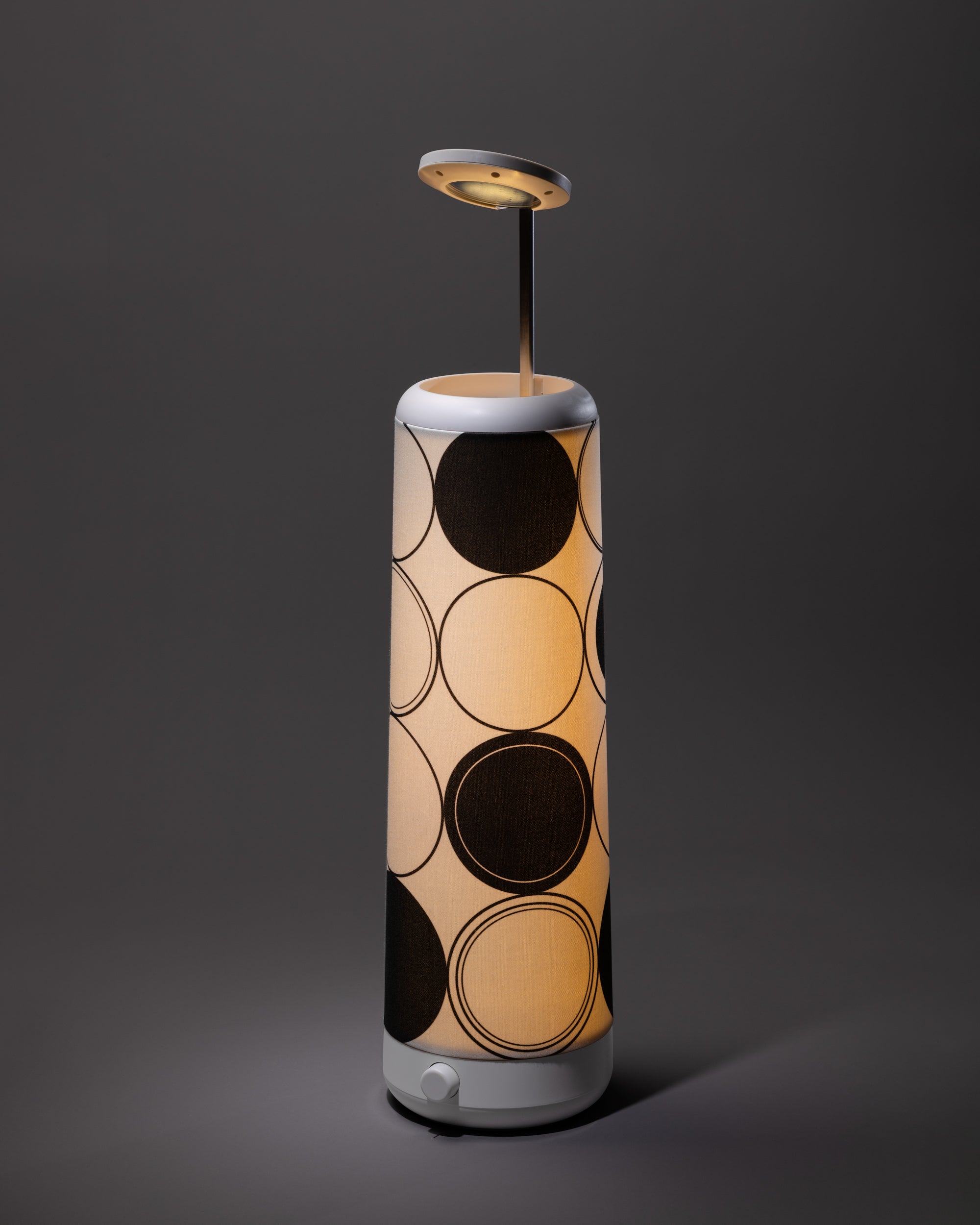 The Nightside Concentric Circles Cotton Shade (shade only) features large black circles on beige fabric in a modern cylindrical design, offering an interchangeable style. Photographed on a plain gray backdrop.
