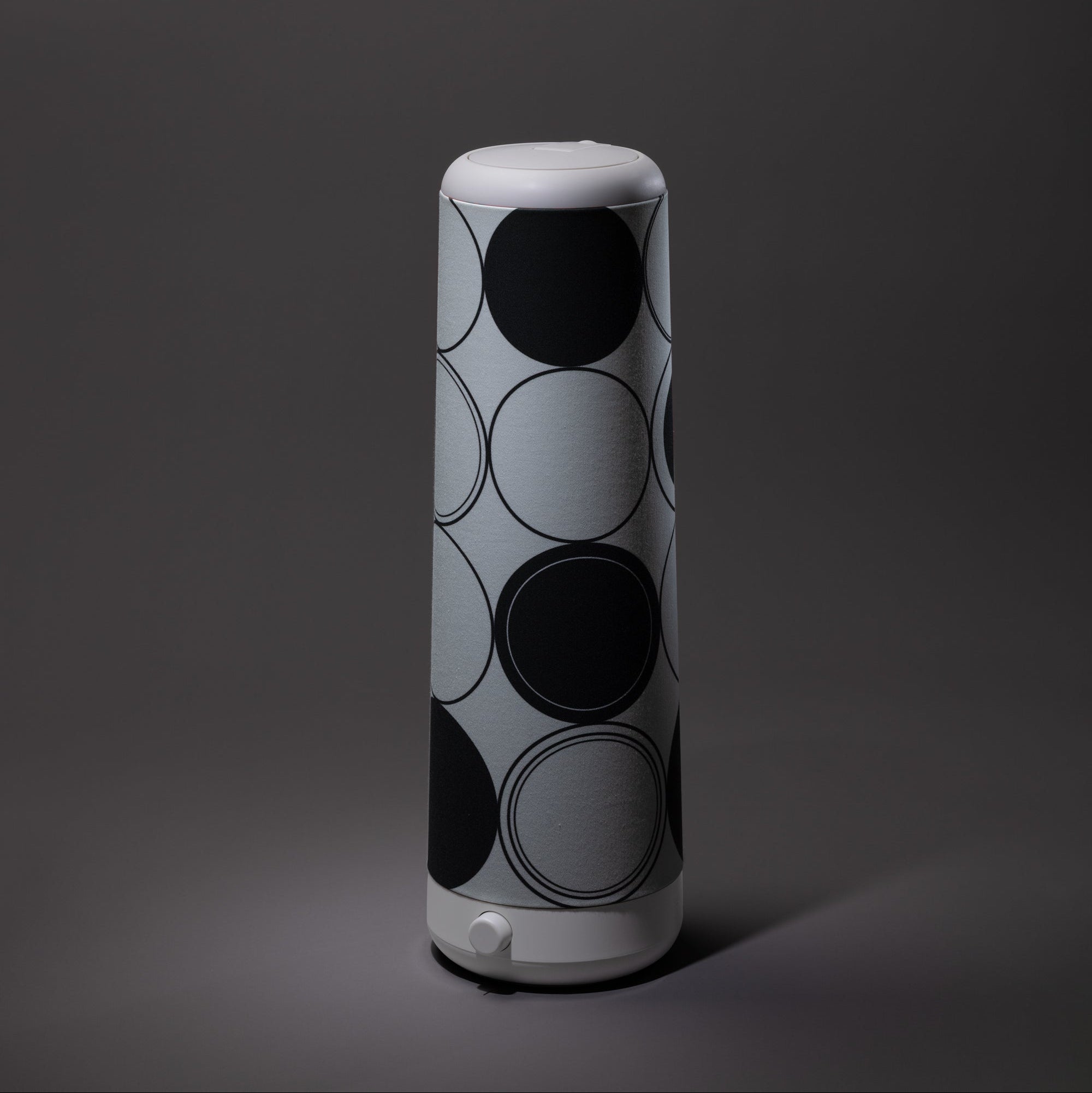 The Nightside Concentric Circles Cotton Shade features a tall, cylindrical design in gray blackout fabric with large black and dark gray overlapping circles on a white-topped and bottomed shade.