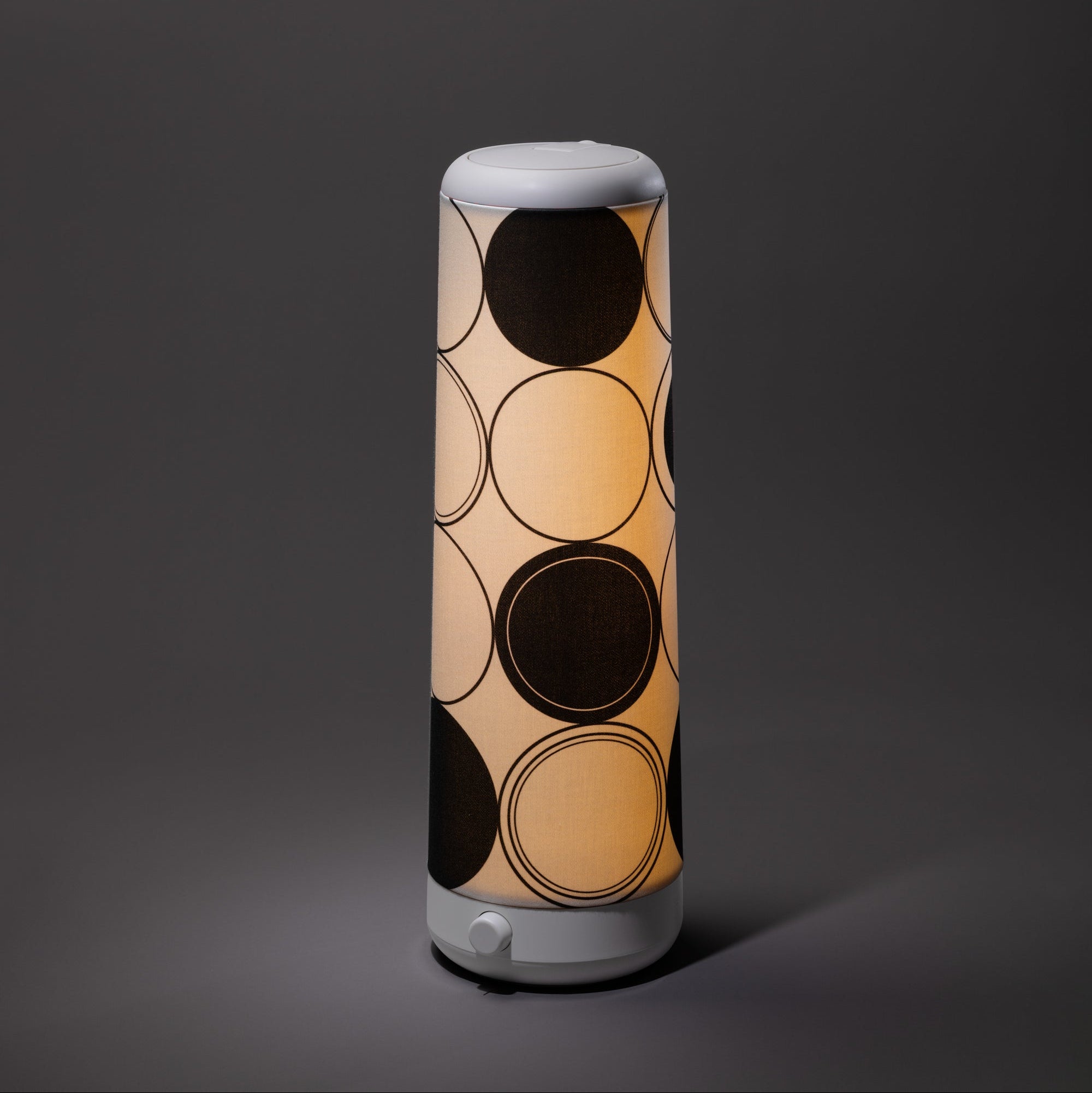 The Nightside Concentric Circles Cotton Shade displays large black circles on a beige background. This cylindrical, patterned shade is interchangeable, making it easy to refresh and match your decor.