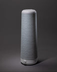 A sleek, cylindrical light grey Cursive Lines Cotton Shade by Nightside with subtle wavy patterns stands on a dark grey background, resembling a modern lamp with interchangeable fabric shades.