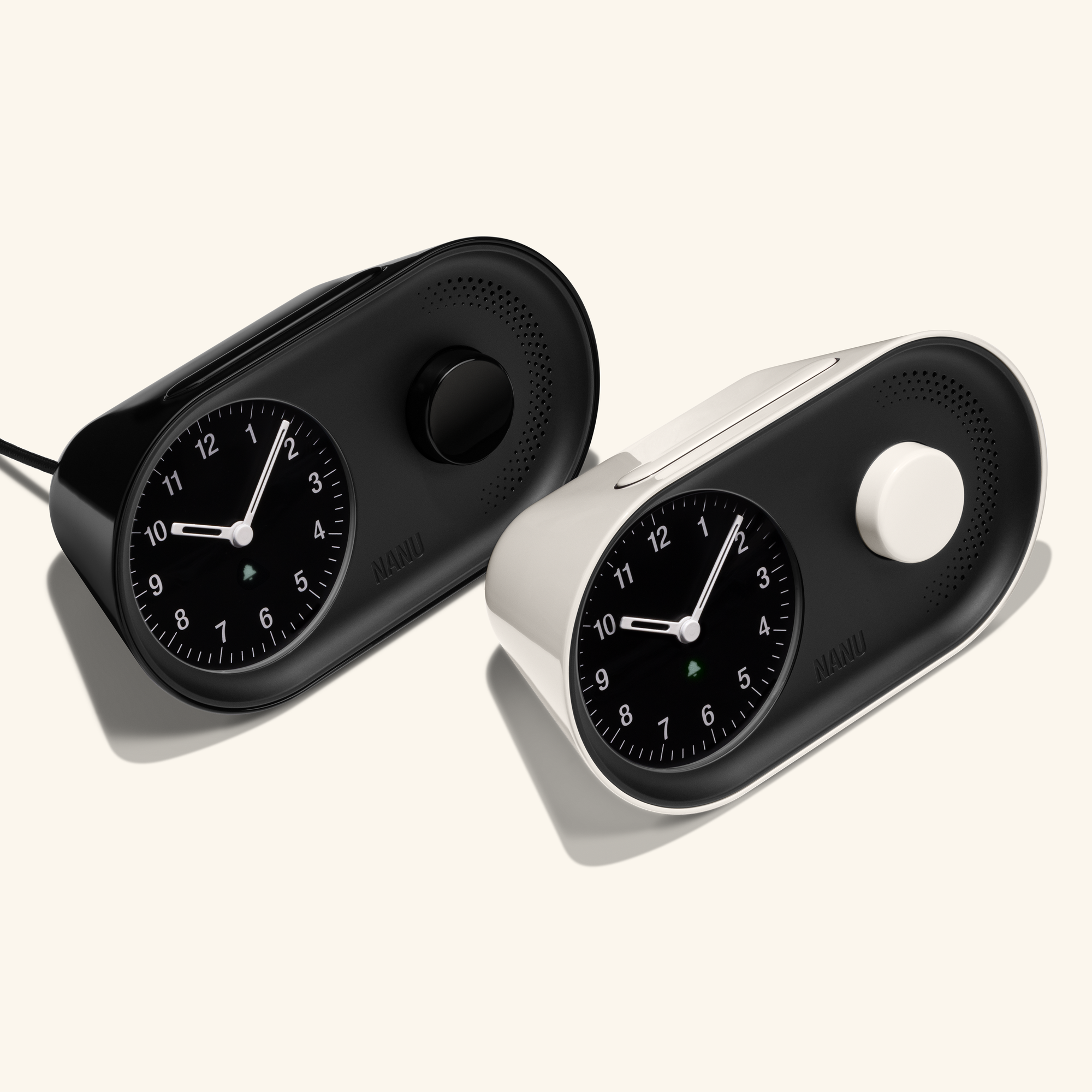 The Nanu Arc Alarm Clock comes in black and white, each with round black faces, white hands, green accents, a side knob, and minimalist wedge-shaped design on a light background evoking precise analog charm.