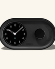The Arc Alarm Clock by Nanu is a sleek black analog-style alarm clock with an analog face on the left and a round speaker grid on the right, displaying 10:11. It features gentle wake-up functionality and has Nanu elegantly embossed below the speaker, embodying timeless style.