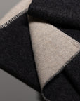 A close-up of the Blacksaw Midnight Sun Throw Blanket, featuring a folded, hypoallergenic wool design with black and beige hues, detailed edge stitching, and soft texture on both sides, set against a plain background.
