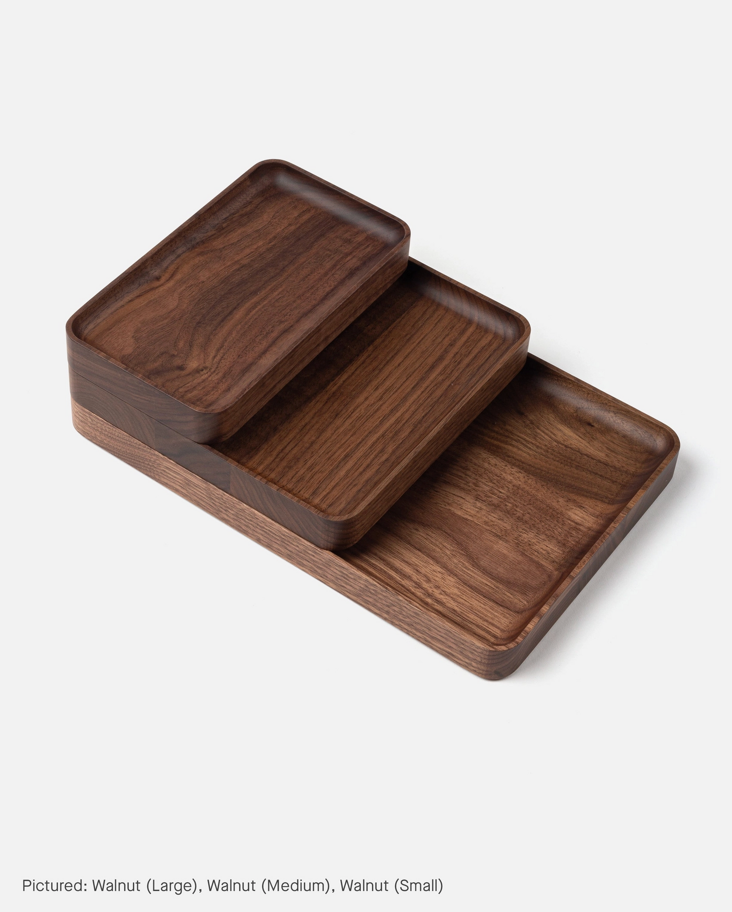 The Ugmonk Valet Tray Bundle features three handcrafted rectangular solid walnut trays in large, medium, and small sizes, stacked in tiers. Each tray showcases smooth corners and a rich dark wood grain on a white background.