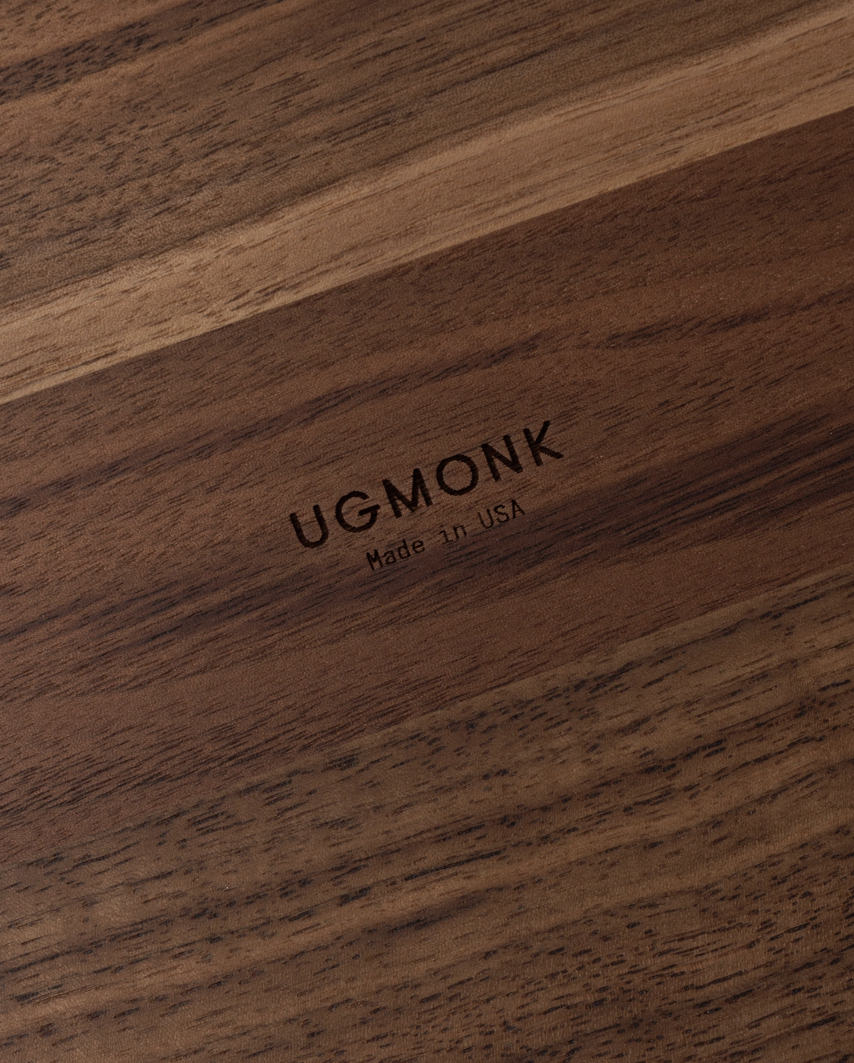 A close-up of a solid walnut surface engraved with UGMONK Made in USA shows a smooth texture and rich natural grain, crafted for the Ugmonk Valet Tray - Walnut Large.