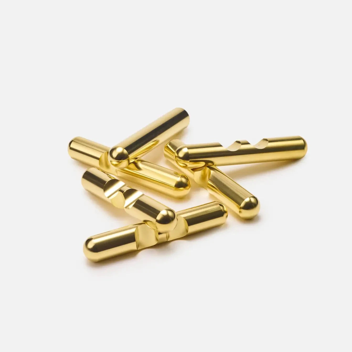 A small pile of Craighill Brass Jack Puzzle pieces rest on a white background. These gold-colored, solid brass plugs have a shiny metallic finish with a cylindrical shape and split pin design, perfect for audio connections, each measuring 1/2 in diameter.