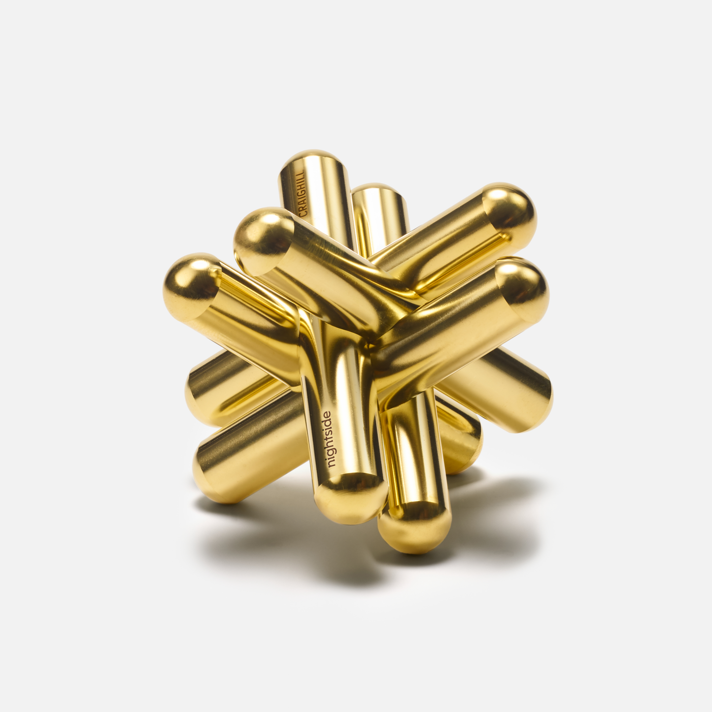 The Craighill Brass Jack Puzzle features intersecting cylindrical rods of solid brass, each with a 1/2 diameter, forming a complex 3x3x3 geometric structure. The gold surface is shiny and reflective, set against a plain white background.