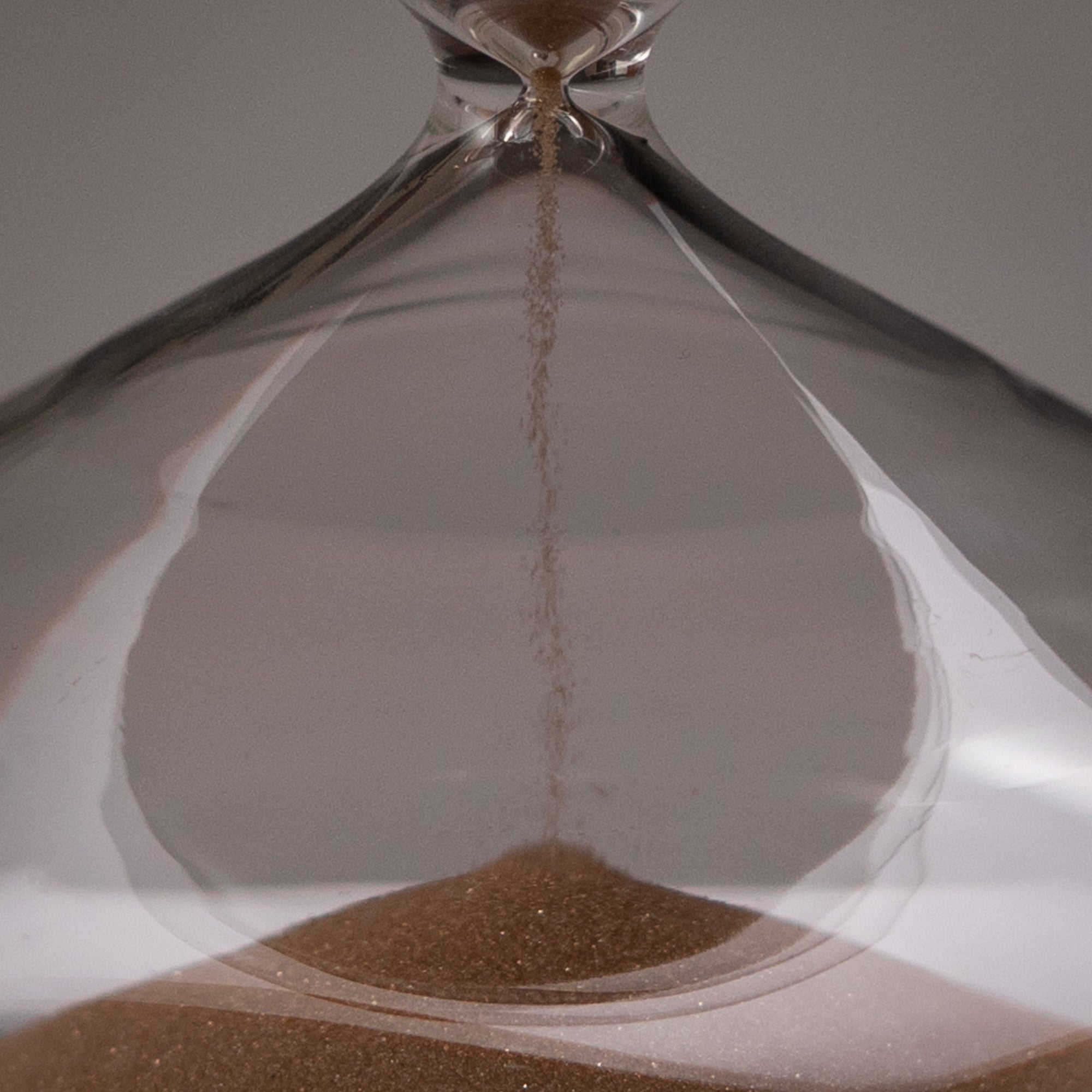Close-up of the Intelligent Change Mindful Focus 30 Minute Hourglass, with sand trickling through its narrow center into a small pile below. The sharp focus and neutral background highlight its symbolism of mindful attention.