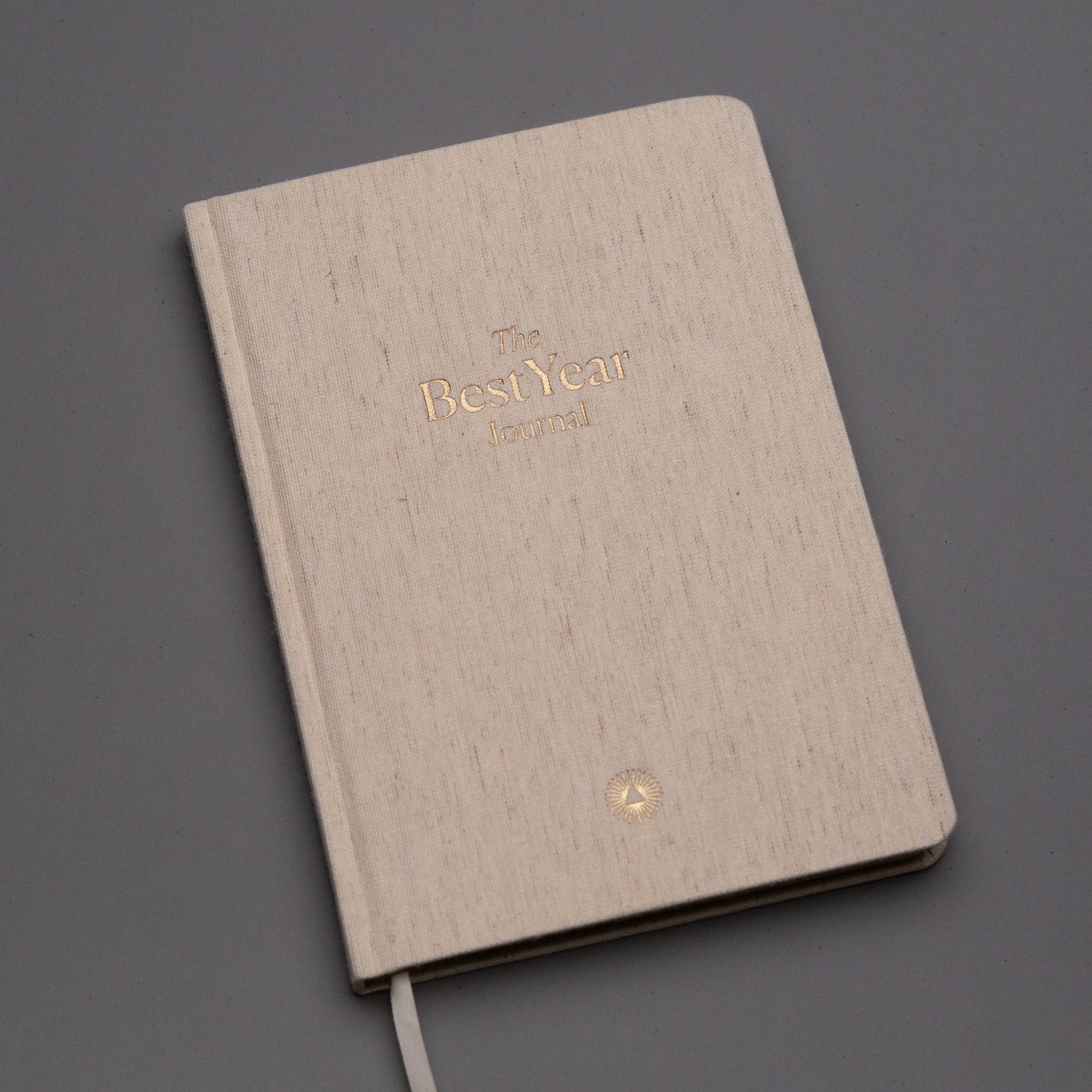 The Best Year Journal by Intelligent Change is a beige hardcover planner with gold embossed text and a white ribbon bookmark—ideal for yearly planning and intention setting.