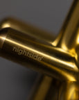 Close-up of intersecting gold metal rods with nightside engraved on one, set against a softly blurred gray background, showcasing sleek modern design.