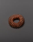 A small, circular copper wire coil is placed on a plain, dark gray surface. The tightly wound coil forms a donut-like shape, with evenly spaced loops creating an industrial, textured ring.