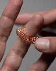 A close-up of a hand slipping a metallic acupressure massage ring onto a finger, with another hand steadying the ring for gentle pressure against a neutral background.