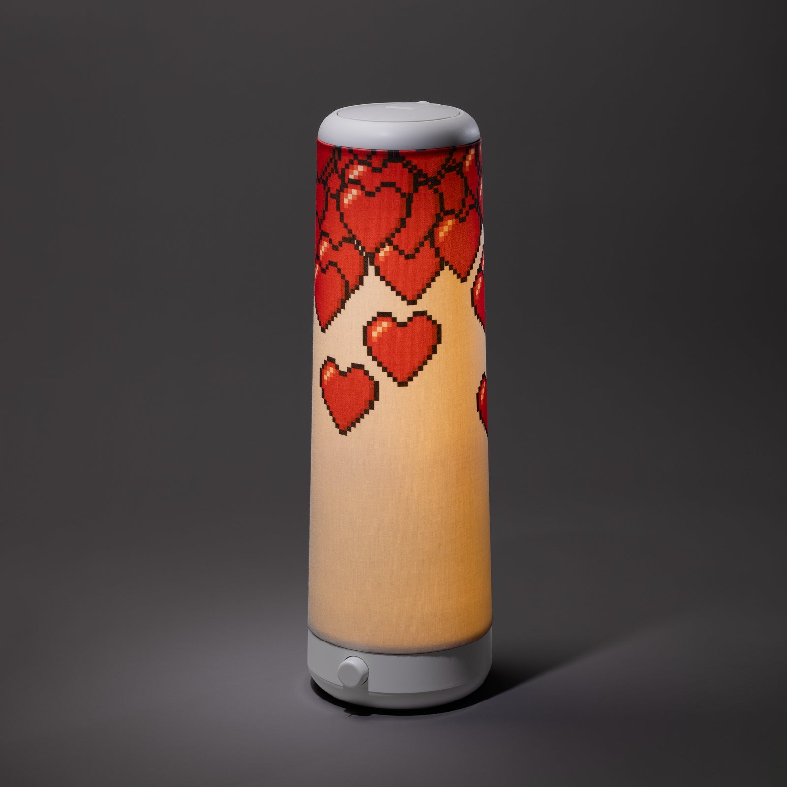 The Nightside NS01 Personal Task Lamp features a cylindrical design with a white base and shade, adorned with red pixelated hearts cascading from the top, casting soothing warm-white LED light against a dark gray background.