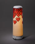 The Nightside NS01 Personal Task Lamp features a cylindrical design with a white base and shade, adorned with red pixelated hearts cascading from the top, casting soothing warm-white LED light against a dark gray background.