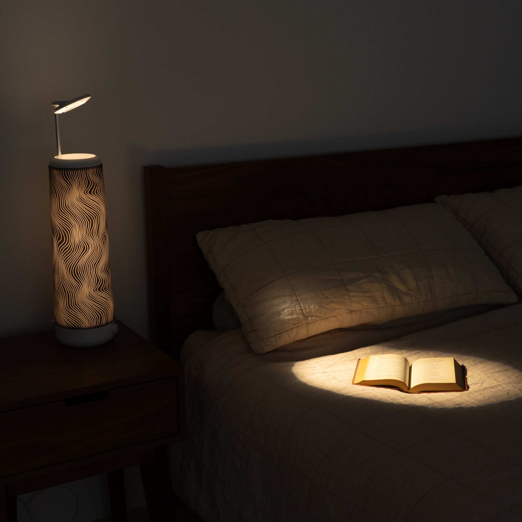 A dimly lit bedroom features a closed book on the bed, softly illuminated by a Nightside Electric Flow Field lamp with its wavy pattern. The cozy atmosphere is enhanced by the wooden headboard, nightstand, and blackout shades.