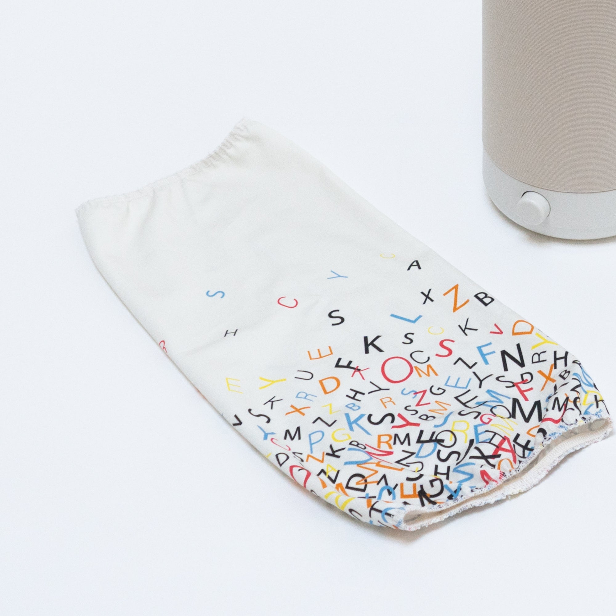 The Nightside Alphabet Cascade Cotton Shade is a colorful fabric cover with scattered black, red, blue, and yellow letters on white. It lies next to a Nightside NS01 task lamp.