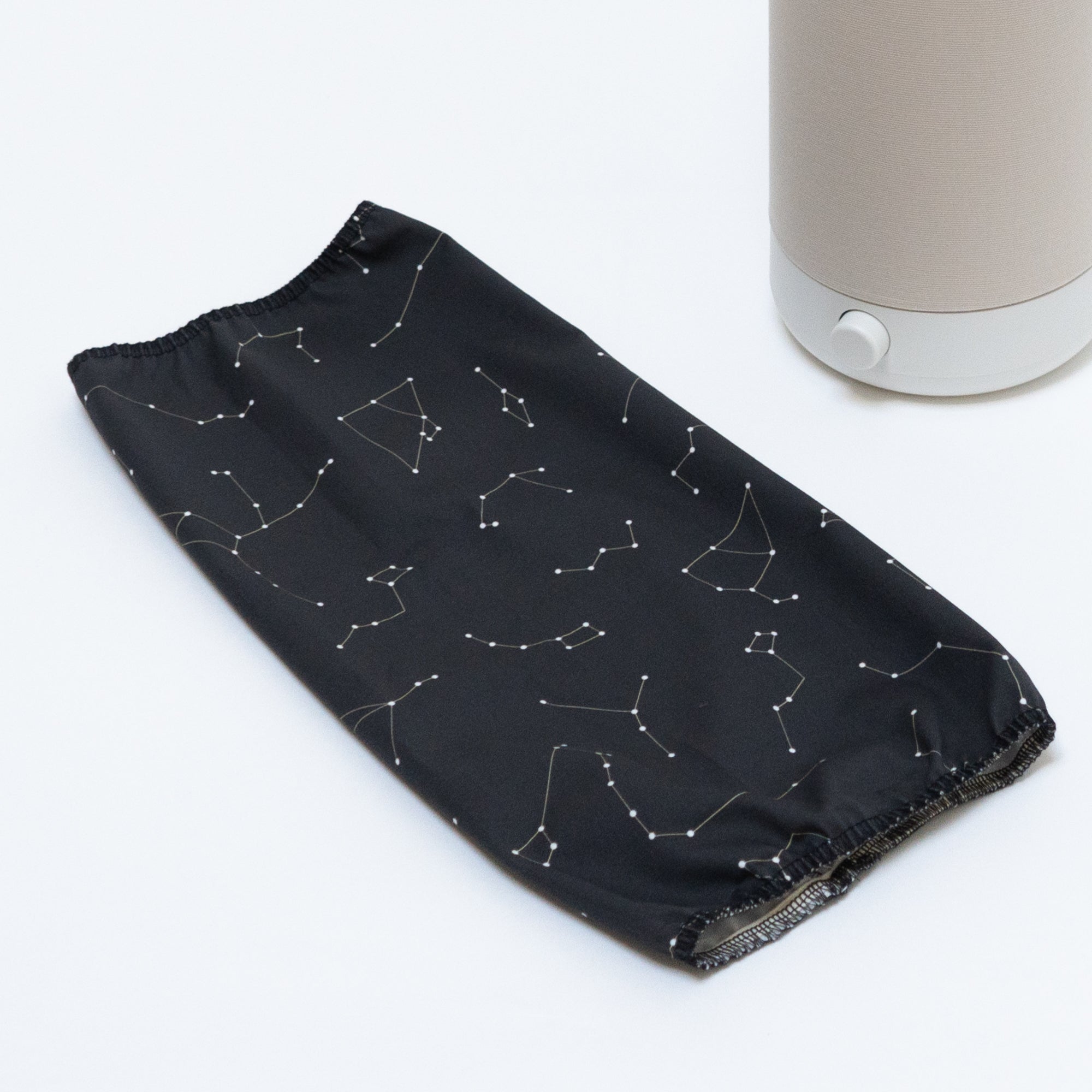 A Nightshade Starlight Cotton Blackout Shade by Nightside, with a constellation pattern, rests on a white surface next to a Nightside NS01 task lamp.