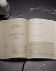 An open copy of The Stoic Journal by Intelligent Change rests on a dark surface beside a small white bust. The visible pages present daily reflection prompts and a Marcus Aurelius quote about seeing life anew, encouraging you to embrace Stoic philosophy in your everyday practice.