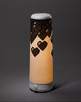 The Nightside 8-bit Hearts Cotton Shade is a cylindrical black lamp with a soft, warm glow and bold pixelated heart patterns near the top against a plain dark background.
