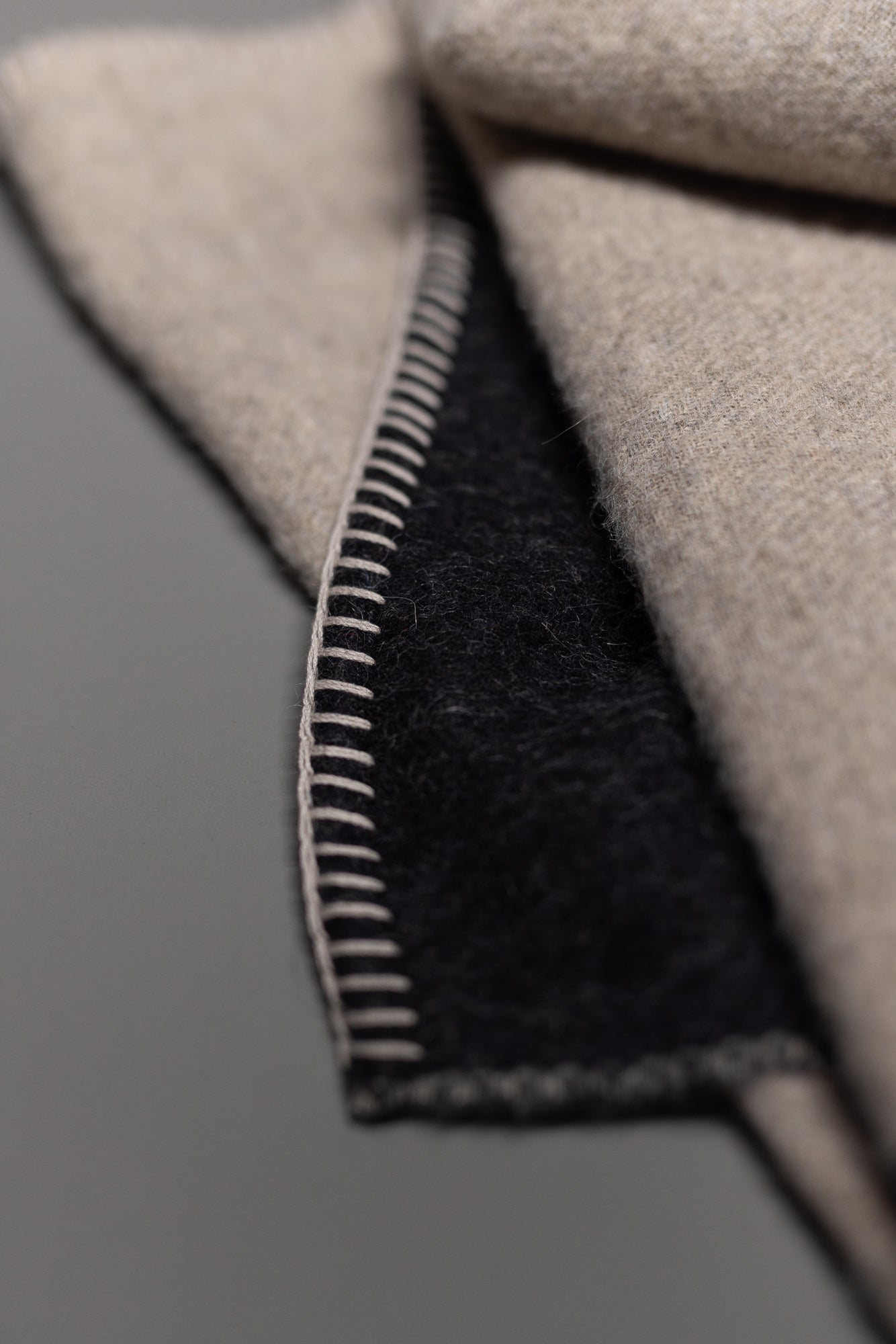 Close-up of the Midnight Sun Throw Blanket by Blacksaw, showing a folded section with a beige outer side, dark inner side, and visible beige blanket stitching. Made from soft, eco-friendly, hypoallergenic Baby Alpaca fiber.