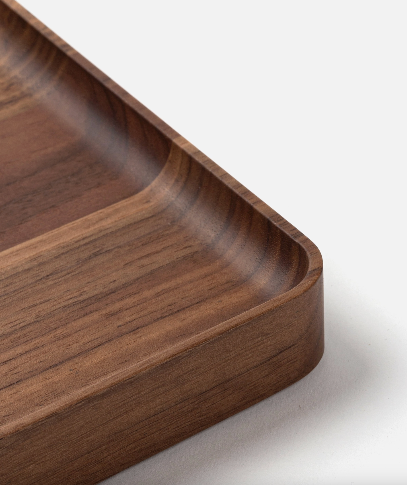 Close-up of the corner of the Ugmonk Valet Tray - Medium, a rectangular walnut tray with smooth, rounded edges and unique grain, displayed on a white surface.